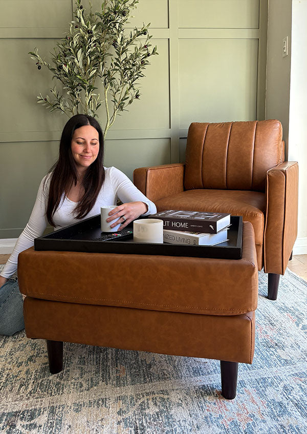 Woman sitting on a brown leather chair with a matching ottoman in a room with green walls and a plant.